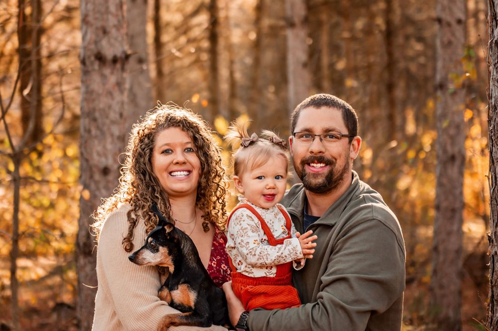 Family sharing warm smiles outdoors in a forest during golden autumn afternoon light.