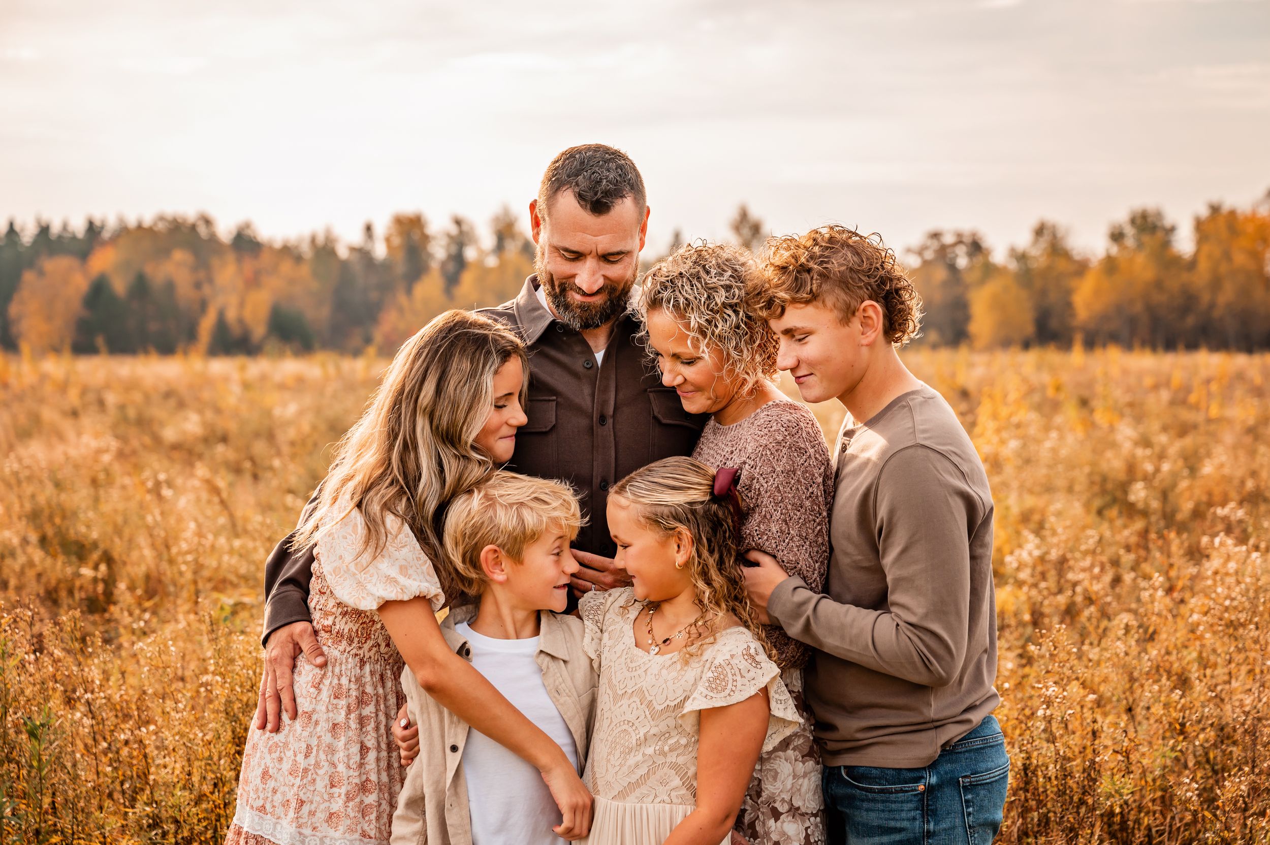 Family embraces together in golden autumn field during sunset photo session.