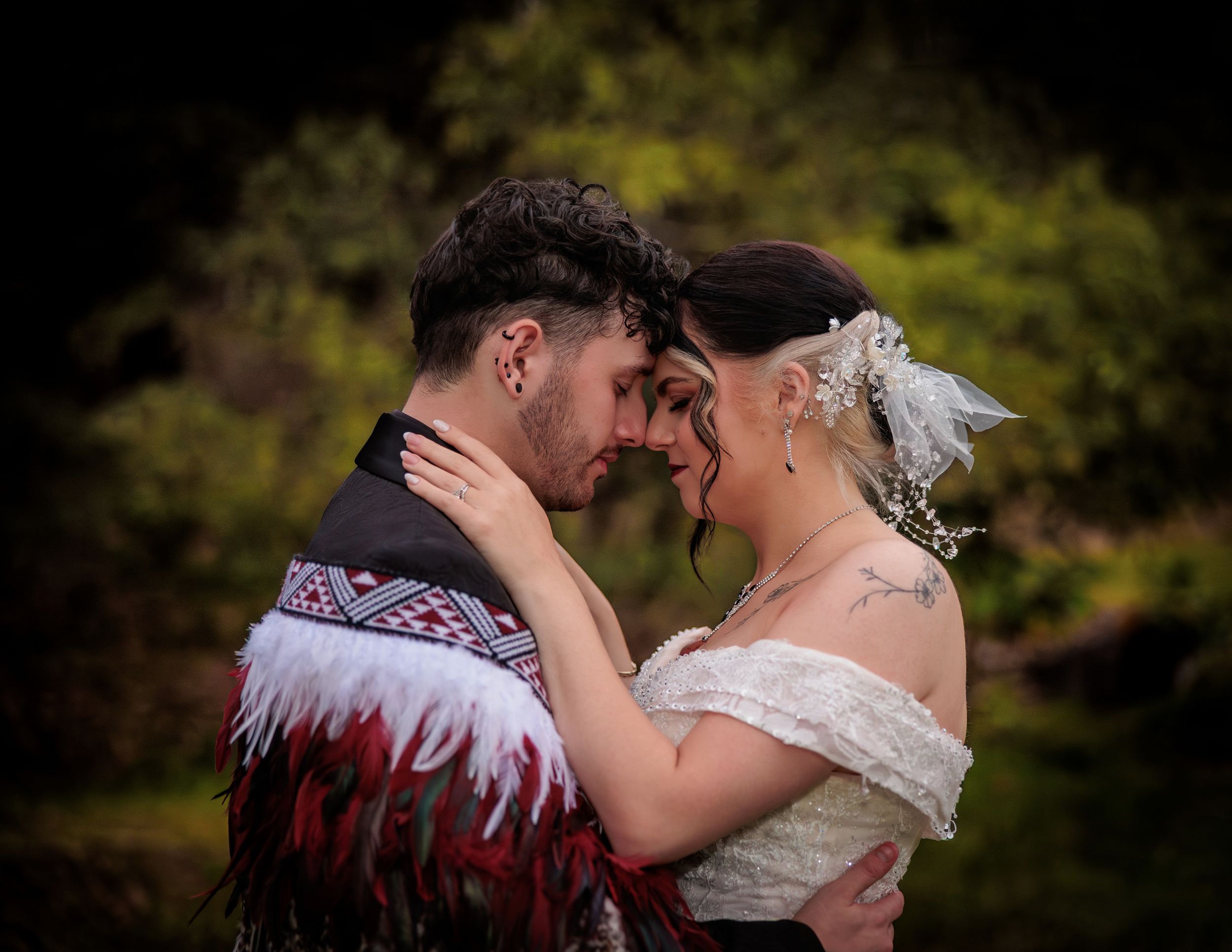 Couple in traditional Maori attire sharing an intimate forehead touch at their wedding ceremony outdoors. Wedding Photography