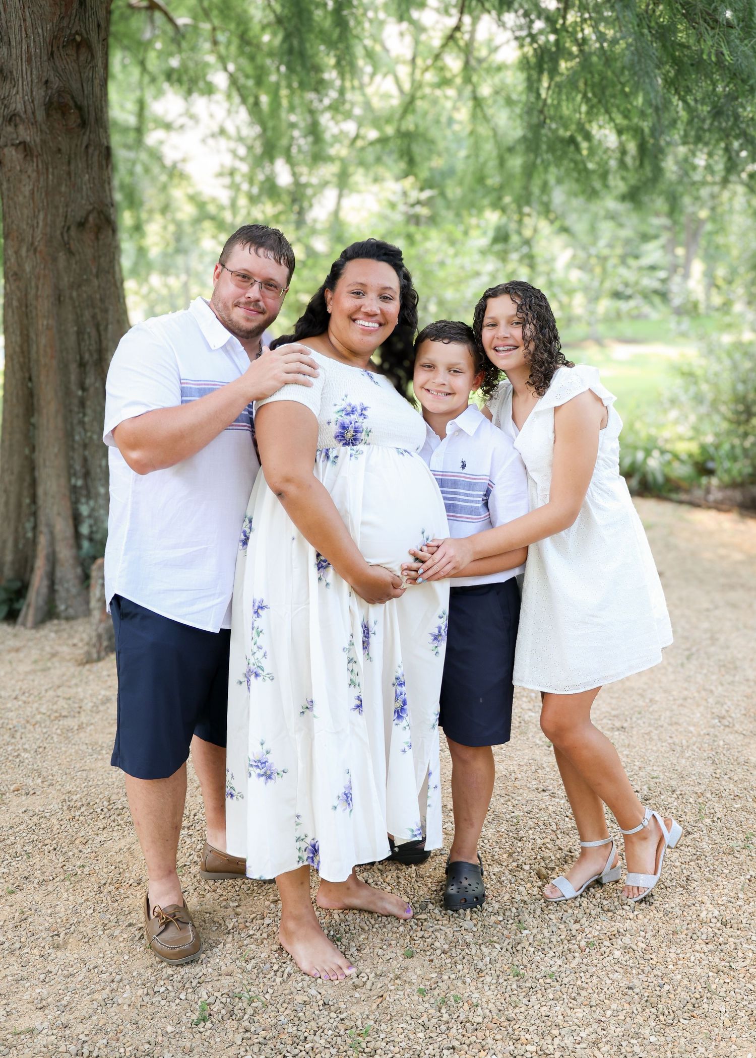 Family photo session with coordinated white outfits captured in natural outdoor setting.