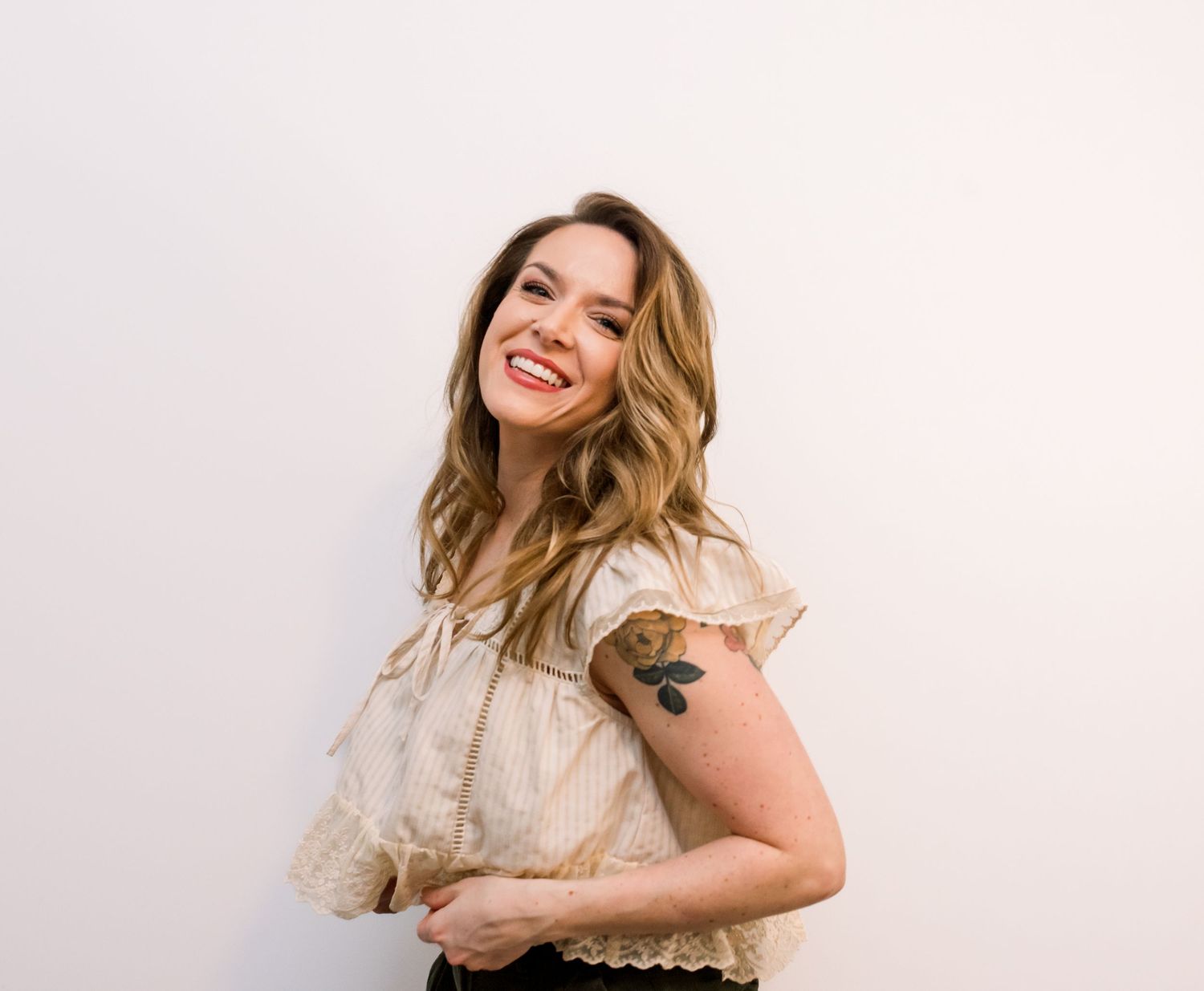 Woman in cream sweater poses casually against white background with natural smile.  Risen Faith Boutique.  Central Indiana. Angela Hartwig.