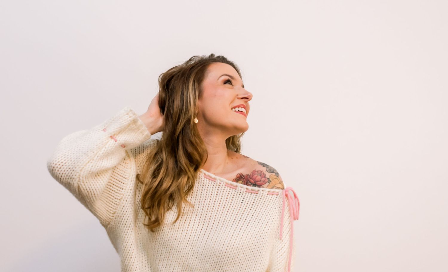 Woman in cream sweater poses casually against white background with natural smile.  Risen Faith Boutique.  Central Indiana. Angela Hartwig.