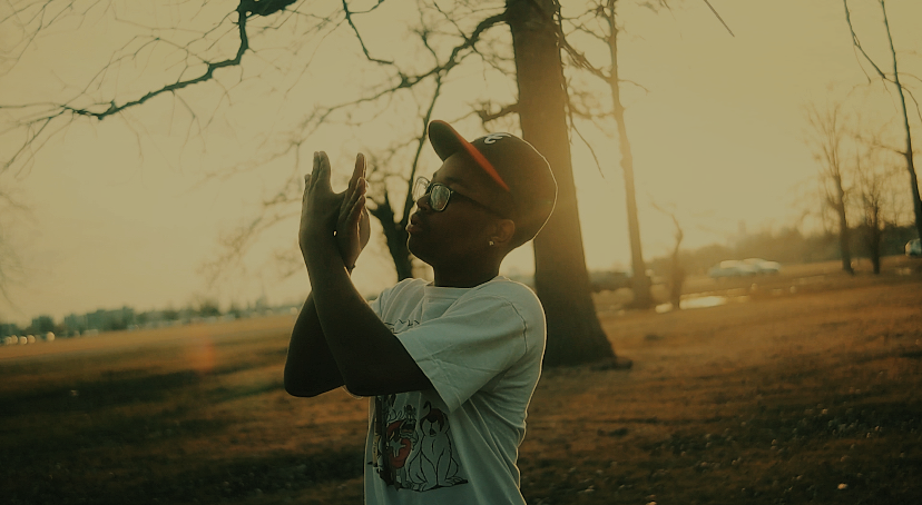A person in a white sweater holds a black dog up towards a golden sunset in a field.