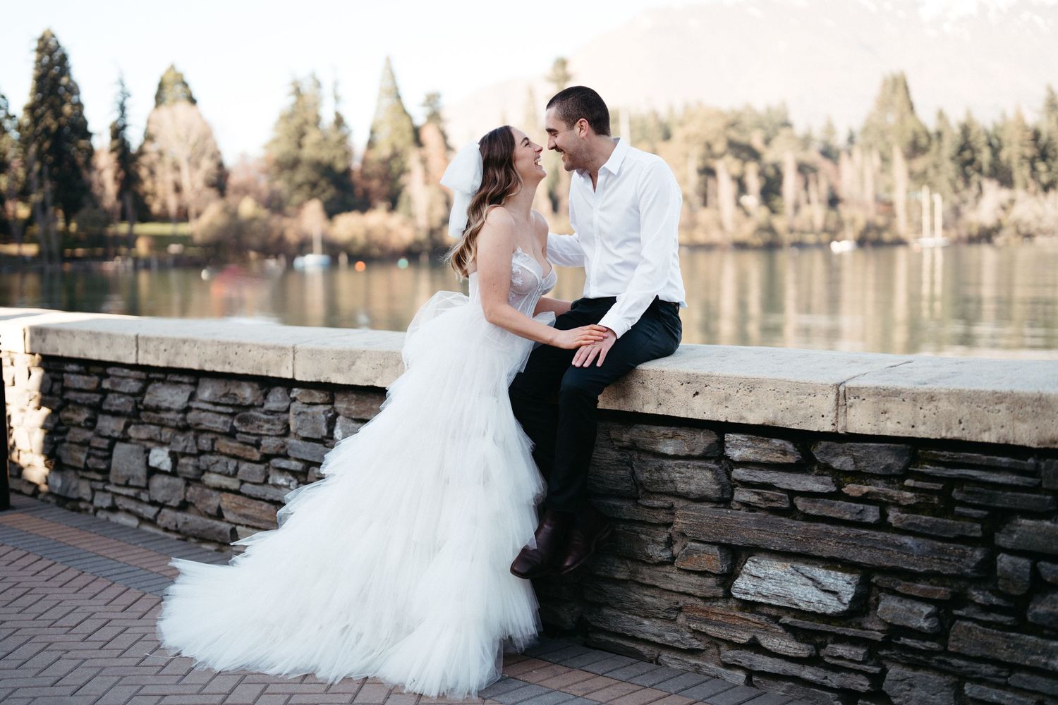 A couple shares a romantic moment on a stone wall overlooking a serene lake.