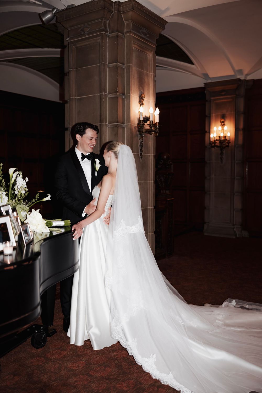 A couple shares an intimate moment at their wedding in an elegant venue with stone columns and wall sconces.