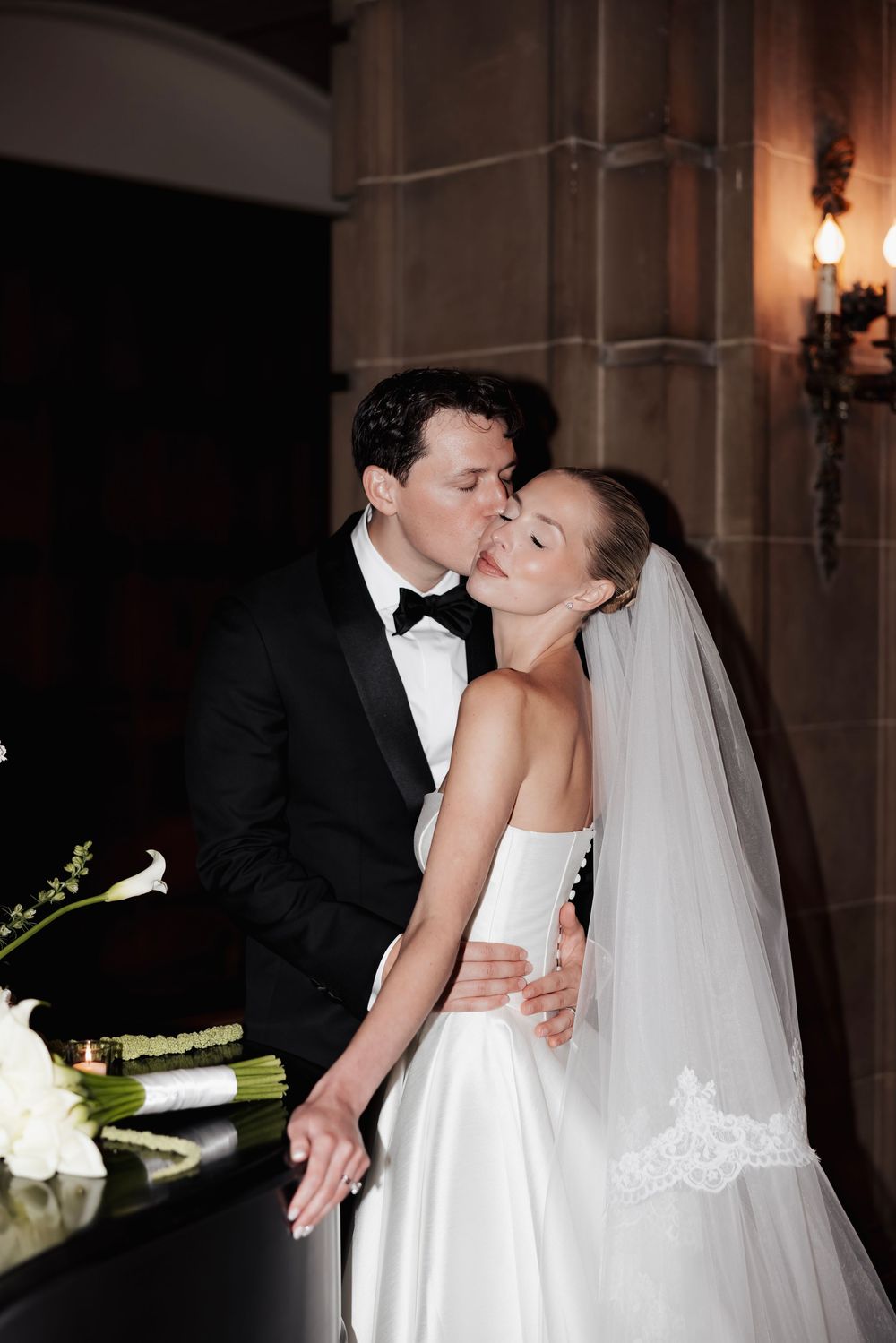 A tender moment between newlyweds at their wedding reception, with the bride in a white gown and long veil.