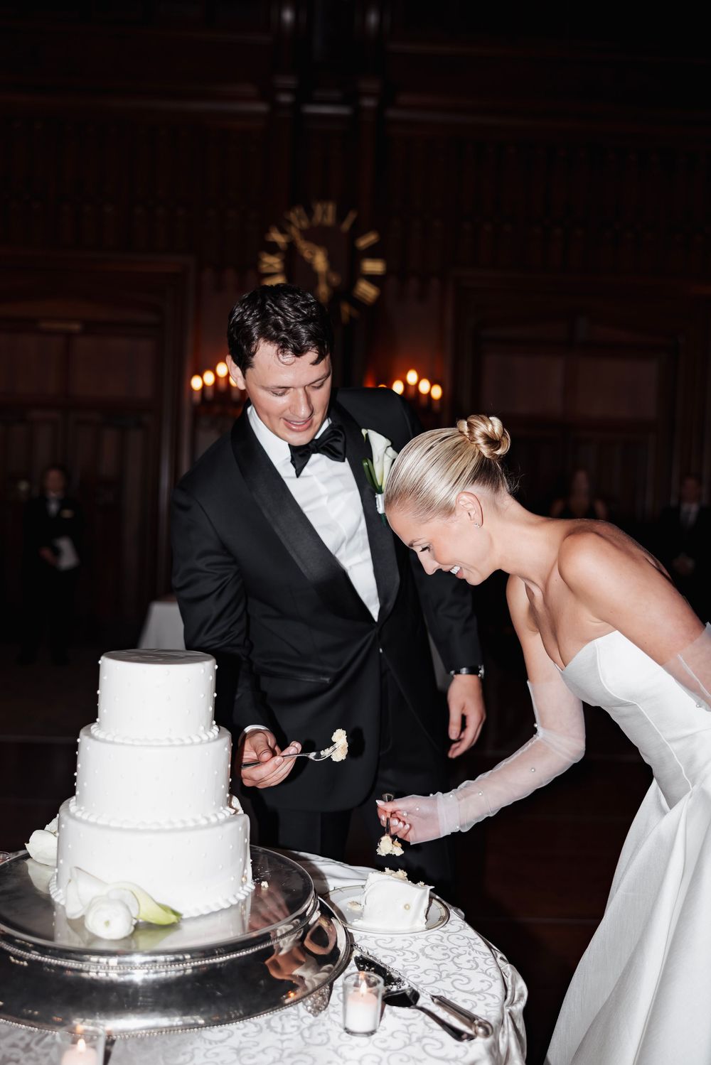 A bride and groom share a playful moment while cutting their elegant white wedding cake at their reception.