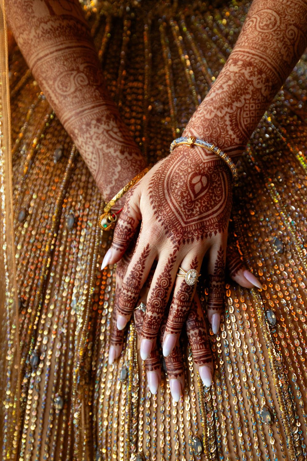 Intricate henna designs adorn hands resting on a sparkly golden sequined fabric.