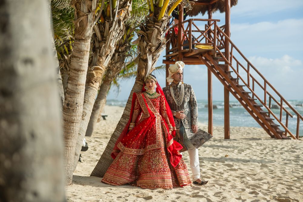 Wedding photo at beach location with couple standing under wooden structure near birch trees.