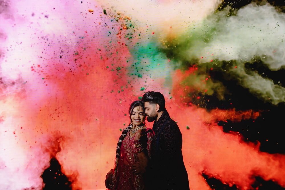 A couple embraces in front of vibrant smoke clouds in pink, red, and turquoise colors during a dramatic photo session.