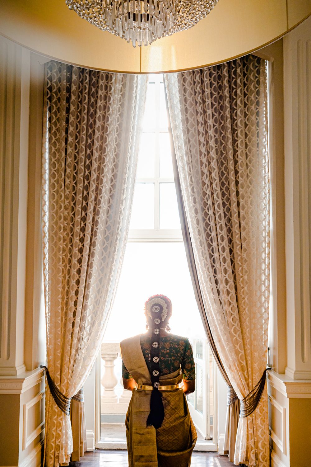 Elegant room interior with crystal chandelier and floor-to-ceiling curtains in warm golden lighting.