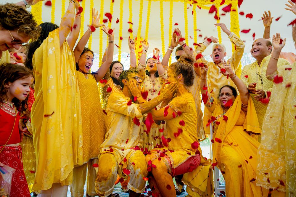 A joyous celebration with people in yellow attire throwing red flower petals during a festive cultural event.