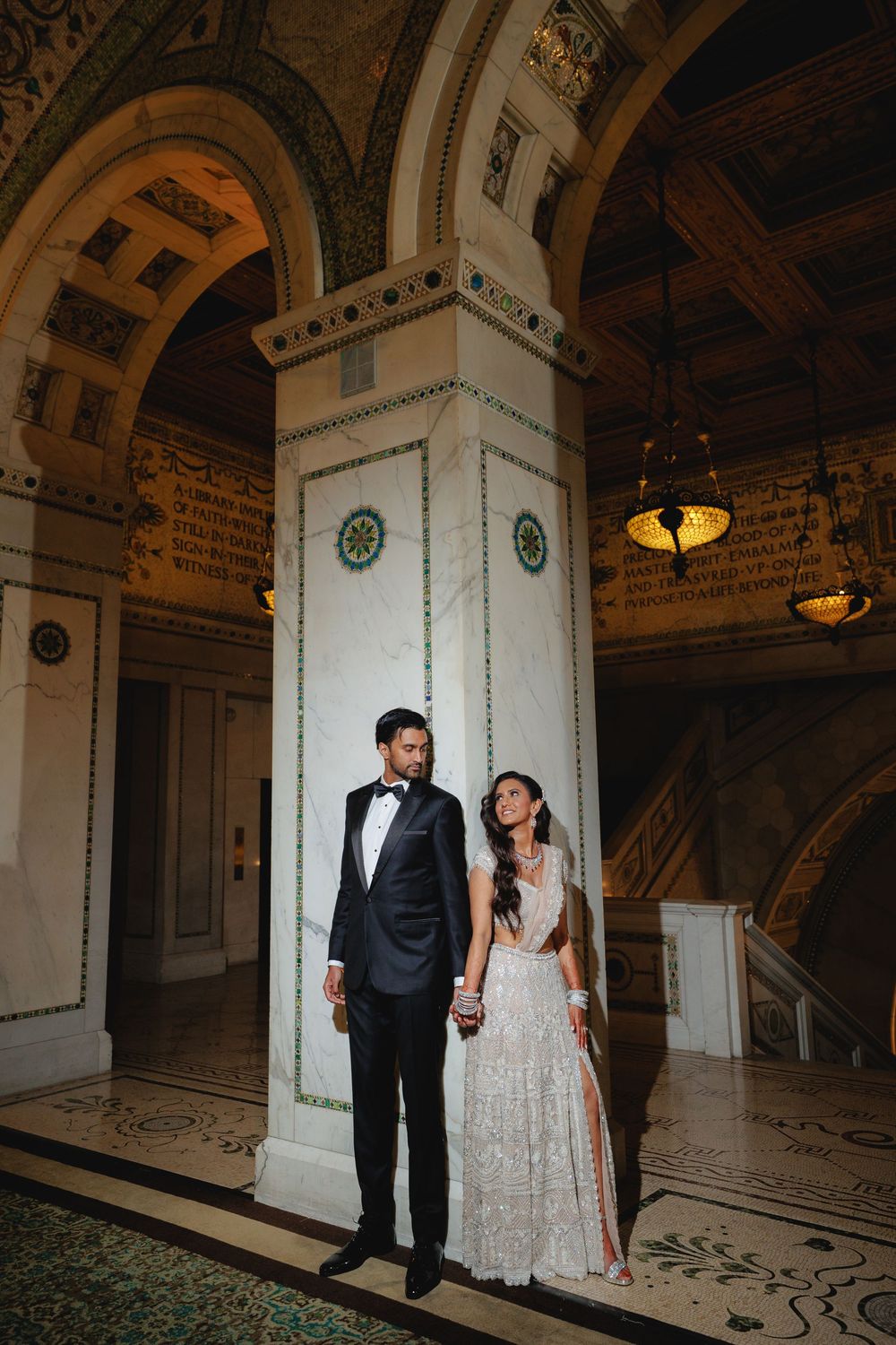 Elegant couple poses in a grand historic building with ornate marble columns and decorative architectural details.