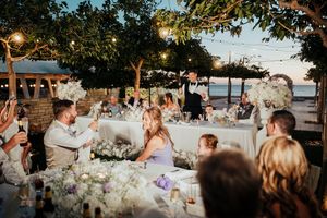 Wedding guests enjoy an outdoor reception dinner under string lights and trees at sunset.