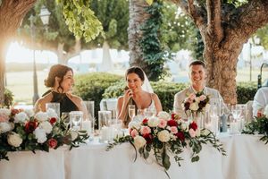 A long wedding reception table decorated with elegant floral centerpieces and greenery garlands under outdoor lighting.