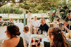 Wedding guests celebrate and dance together during an outdoor reception under string lights and floral decorations.
