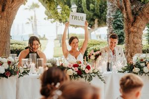 Elegant outdoor wedding ceremony setup with white chairs and floral arrangements under tall trees.