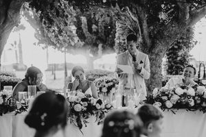 A black and white panoramic photograph shows a group gathered under trees at an outdoor social event.