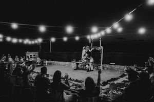 String lights illuminate an outdoor evening event with silhouetted figures gathered beneath a dark sky.