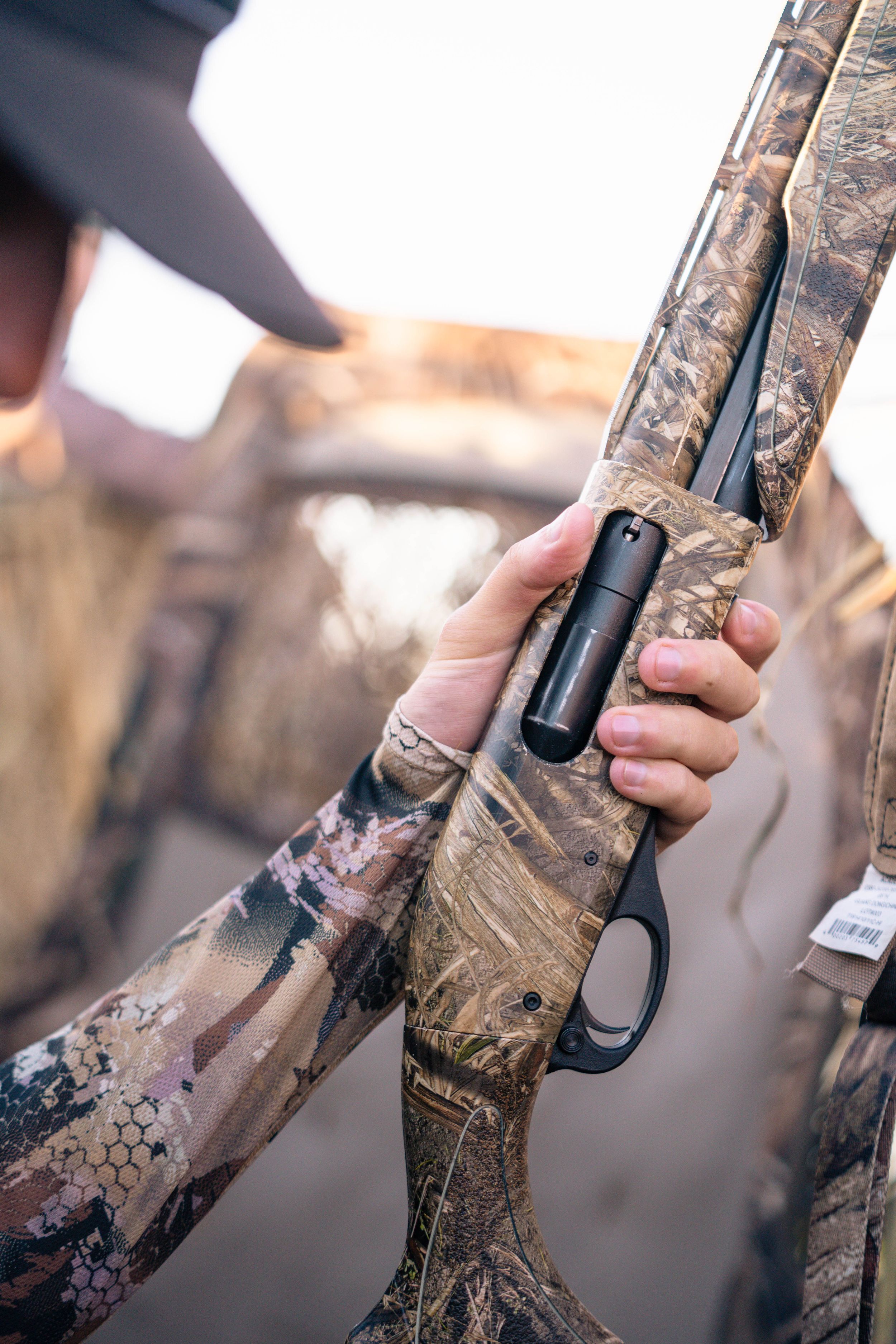 Close-up of camouflaged shotgun being held in hunting blind.