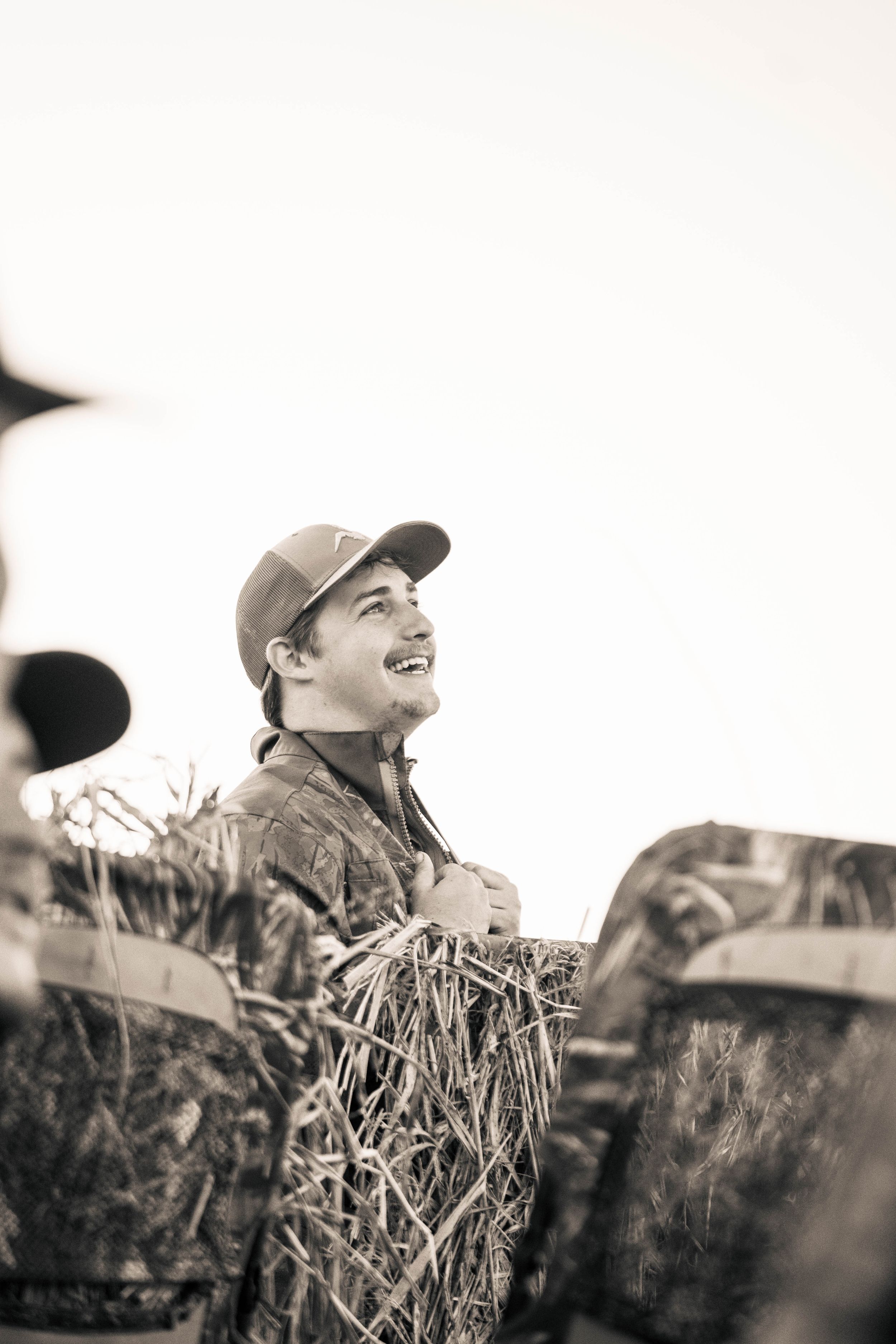 Hunter in camouflage gear smiles while duck hunting in a natural blind.