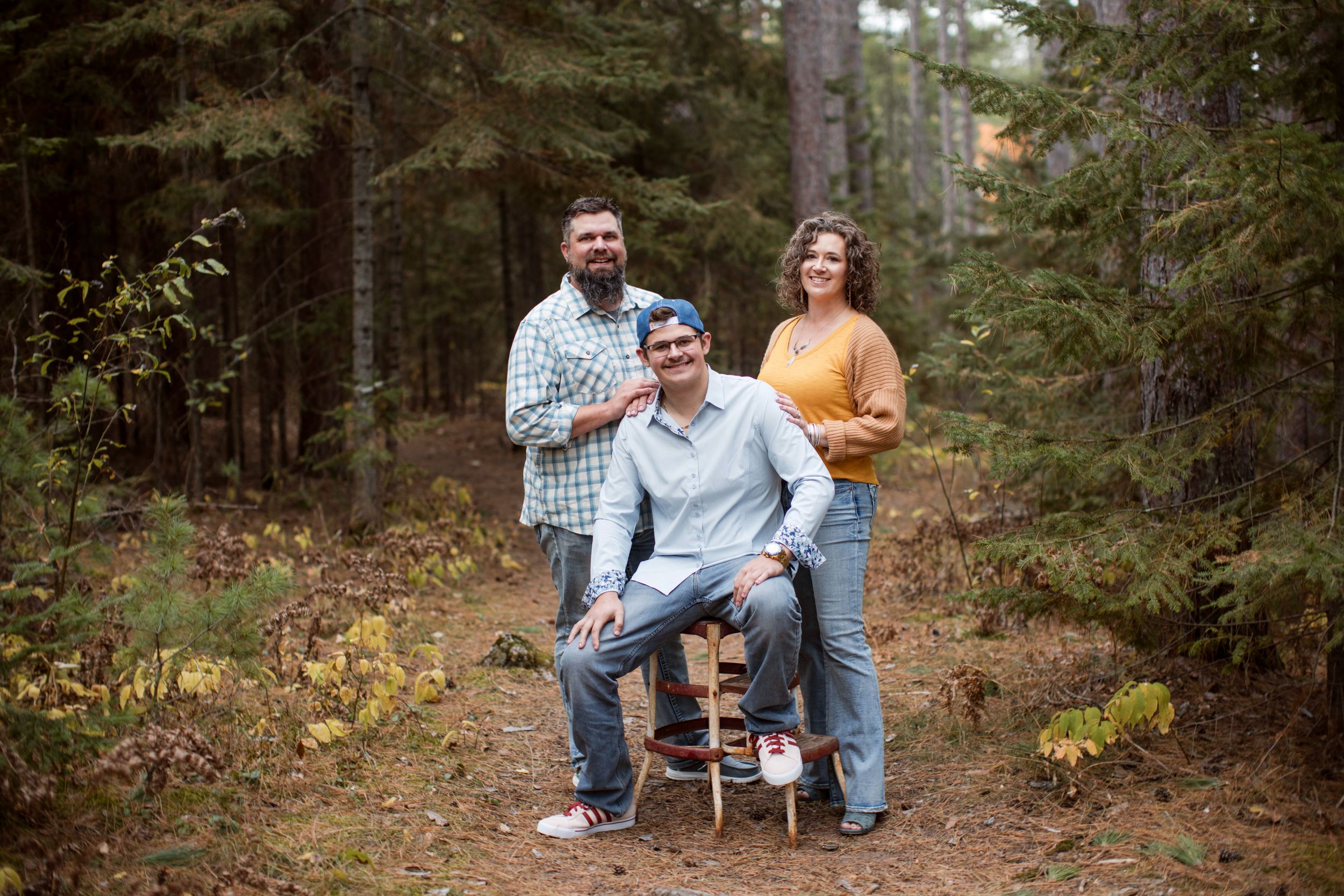 A couple enjoys a romantic autumn photoshoot in a wooded forest setting with fallen leaves.