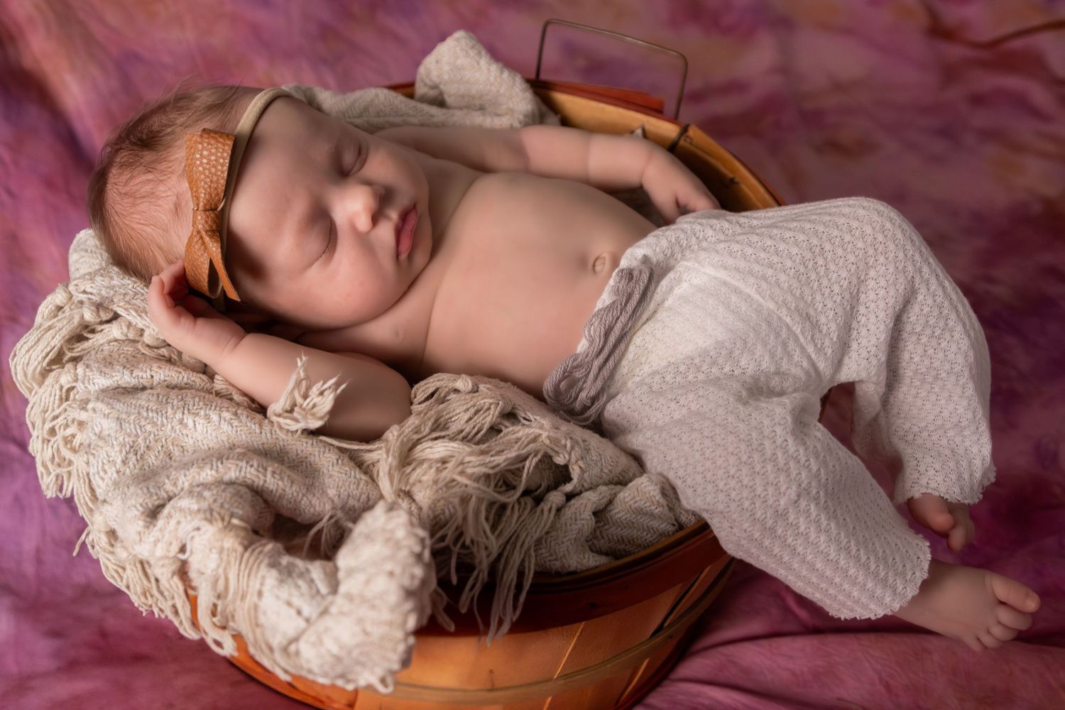 Newborn baby sleeping peacefully on vintage lace textiles with pink toned lighting.