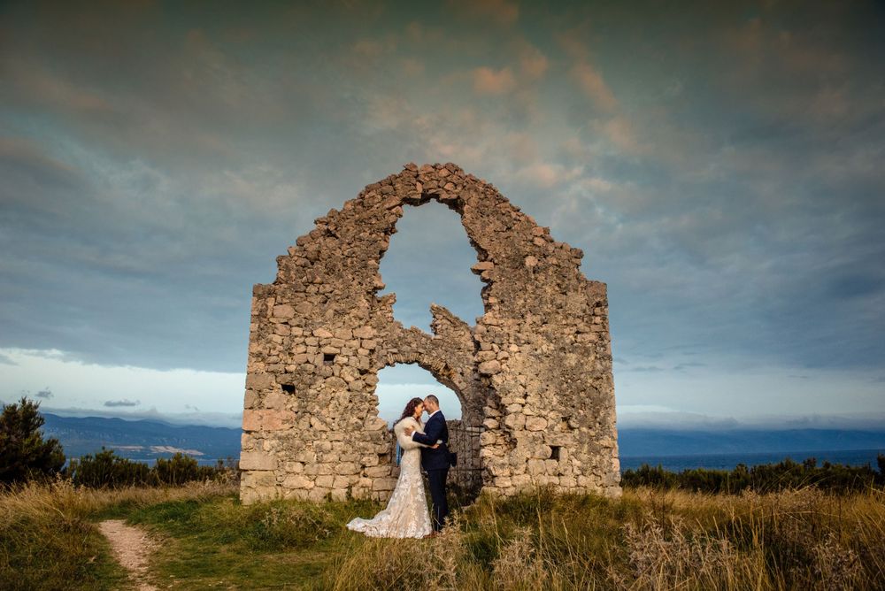 A romantic moment captured at a historic stone church ruin overlooking a dramatic cloudy landscape.