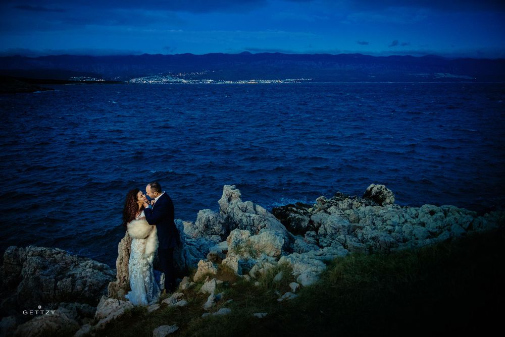 A romantic coastal scene silhouetted against deep blue waters and mountains in the background.
