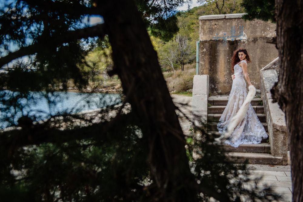 A figure in a white wedding dress stands elegantly in an ancient stone doorway overlooking the Mediterranean coast.