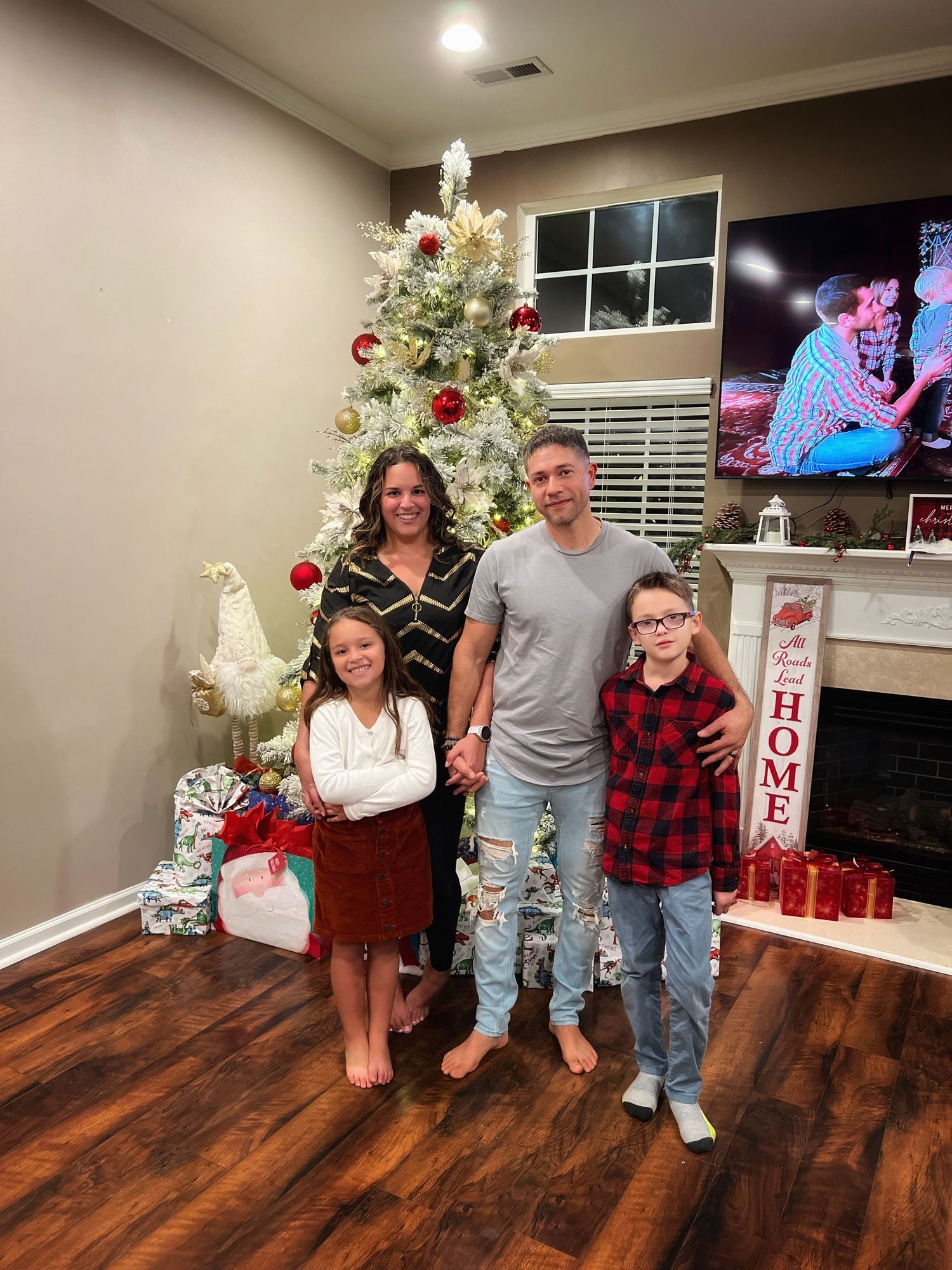 Family poses in front of decorated Christmas tree with presents and holiday decor.