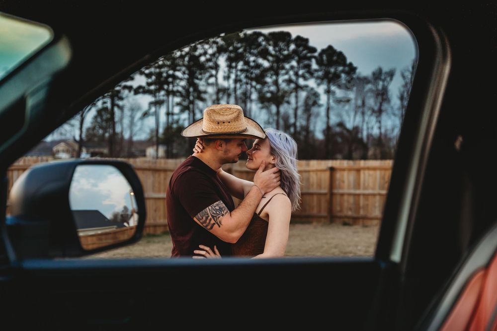 Couple sharing a romantic embrace and kiss viewed through a car window outdoors. Jacksonville, NC