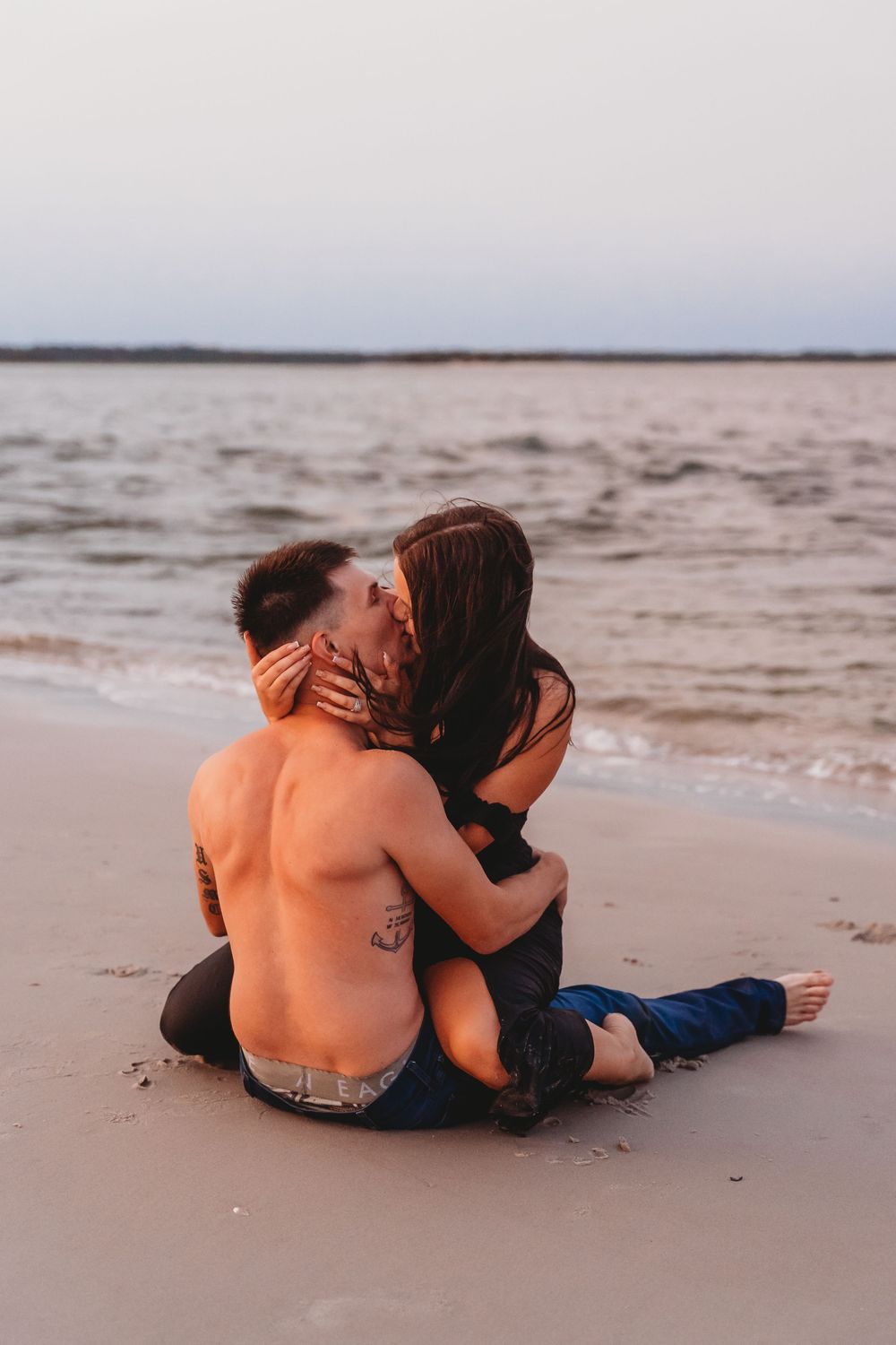 Couple kissing intimately while sitting on a sandy beach at sunset by the ocean. North Topsail Beach photographer