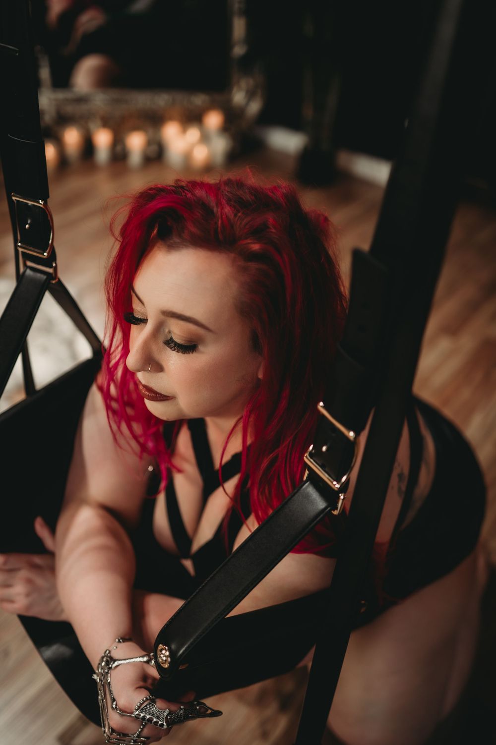 Artistic boudoir photo featuring vibrant red hair and dark attire in moody indoor lighting.