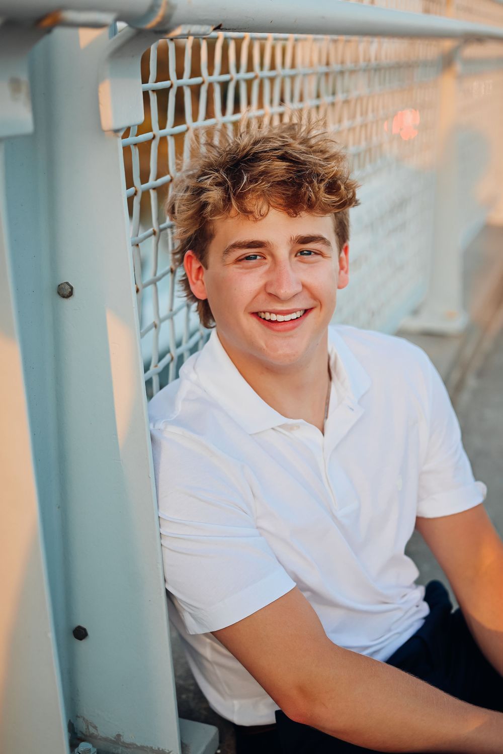 Casual portrait against white railing during sunset with warm lighting. Senior photography