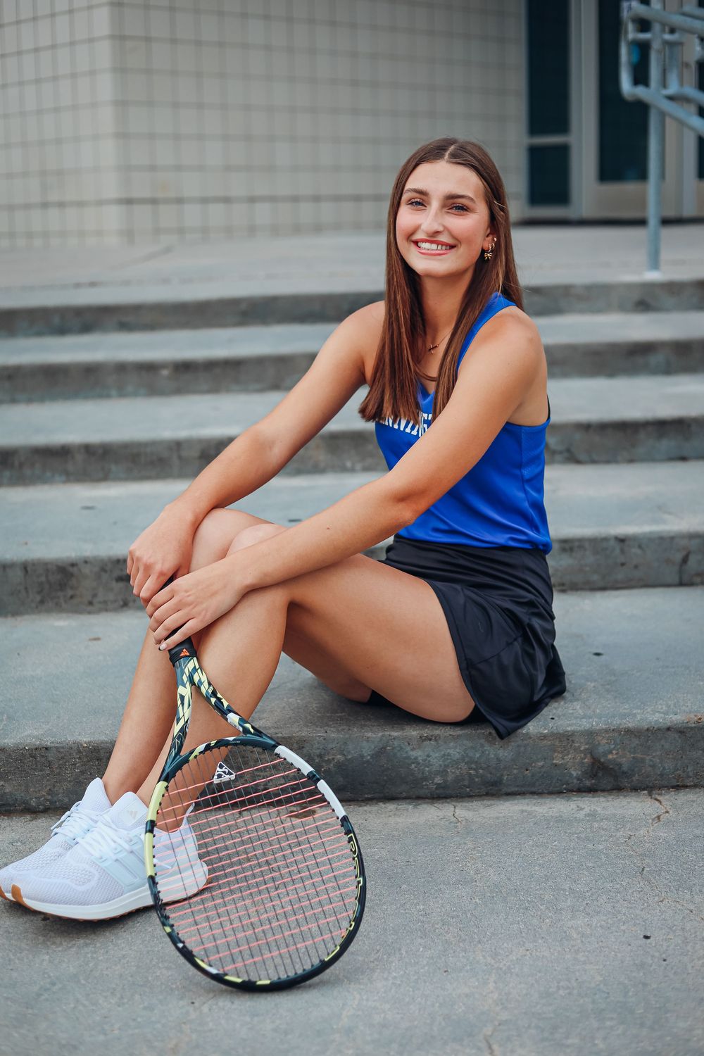 Tennis player sitting on concrete steps with racquet and athletic wear. Senior photography