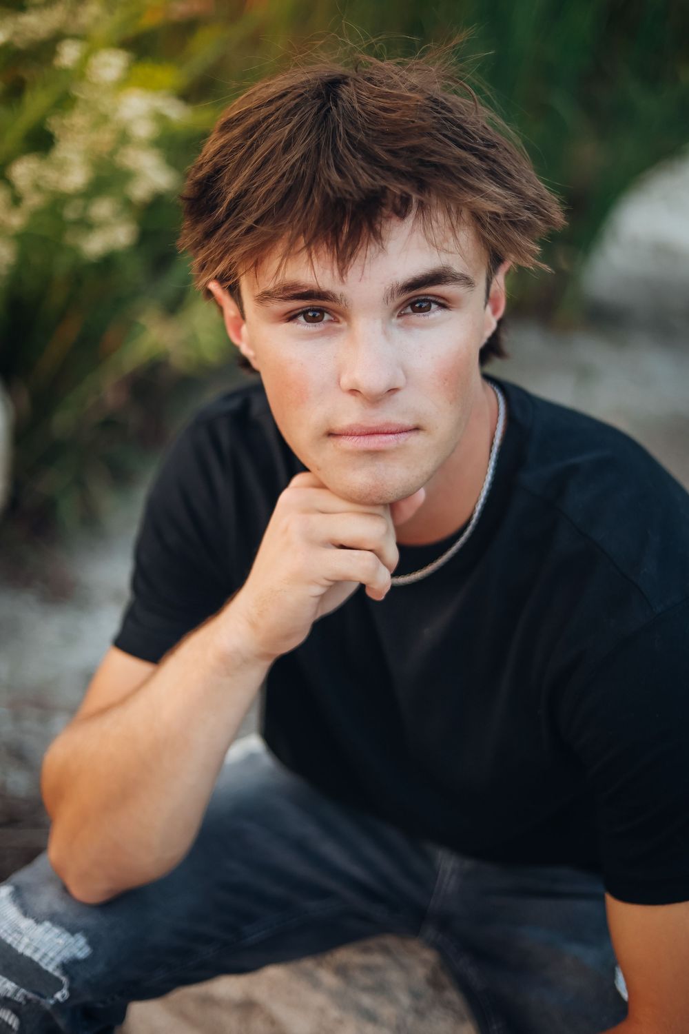 A person in a black t-shirt rests their head on their hand while sitting outdoors in natural lighting.