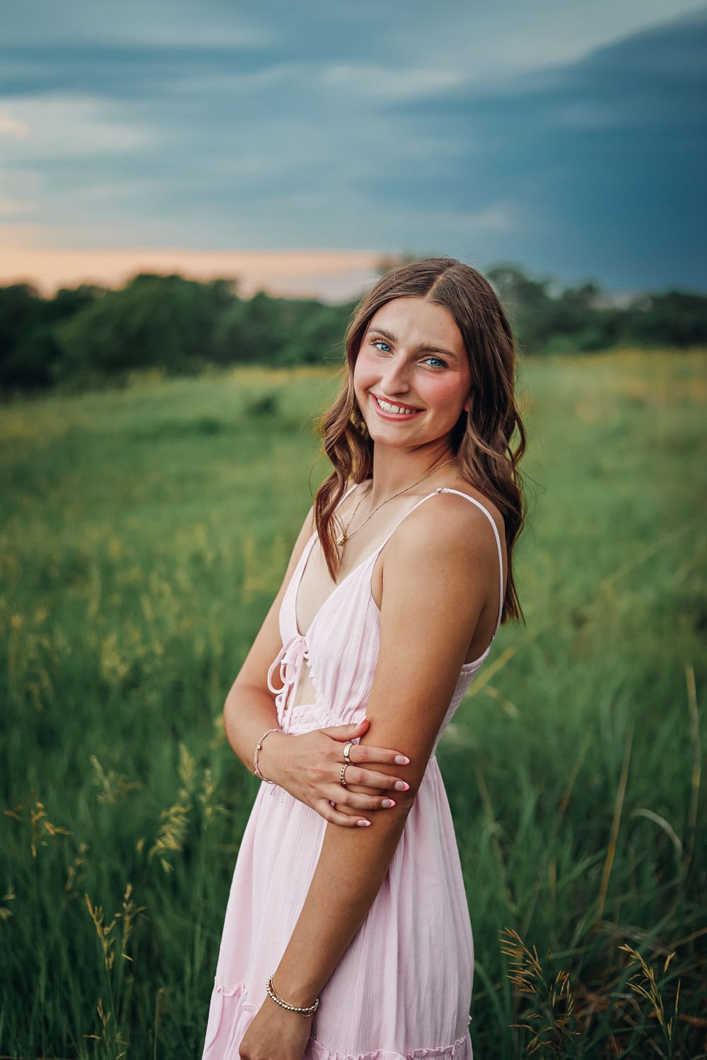 Woman in pink dress poses in a golden field during sunset. Senior photography