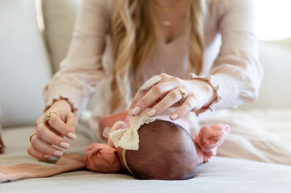 a mother fixing a newborn babies bow. baby is lying on the couch and the focus is on the top of babies head facing mom