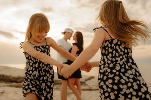 Children in matching floral dresses play together on a beach at sunset.