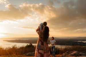 People enjoying a scenic mountain overlook during golden hour sunset with water and landscape views in background.