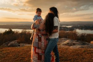 A couple embraces on a hilltop during golden hour sunset with scenic mountain views in the background.