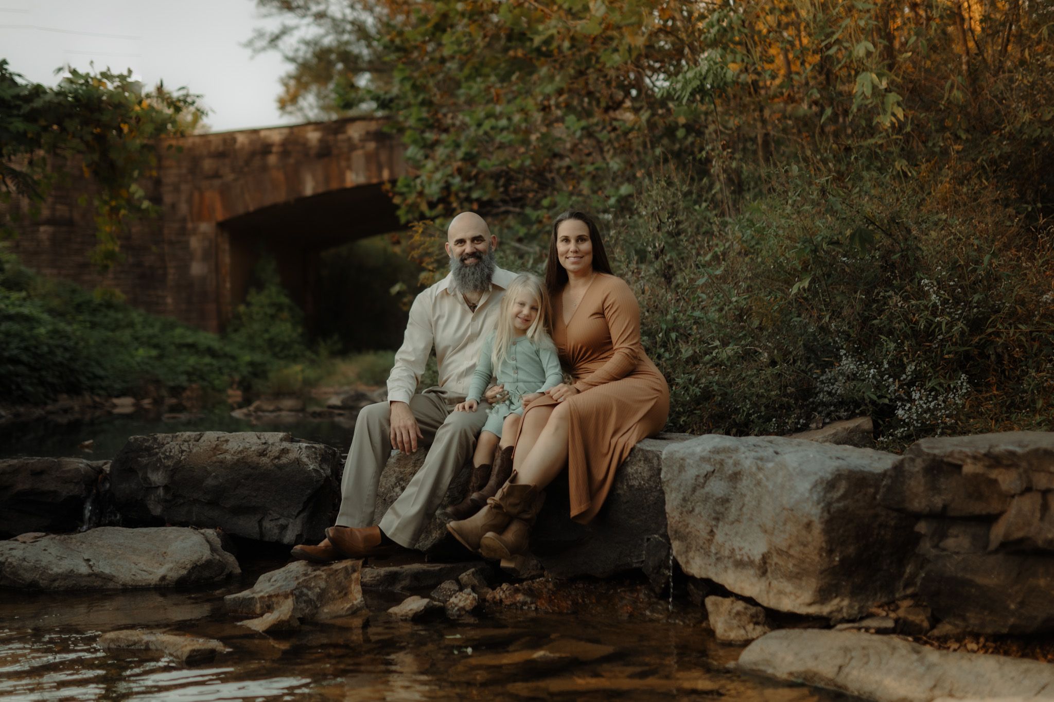 Couple relaxing on stone ledge surrounded by autumn foliage during sunset.