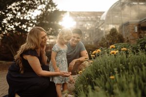 Family admiring yellow flowers in a sunlit garden near a greenhouse, golden hour light glowing warmly behind them.