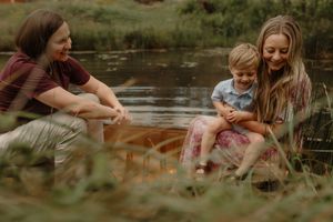 A family enjoys a peaceful moment together by a pond's edge surrounded by tall grass.