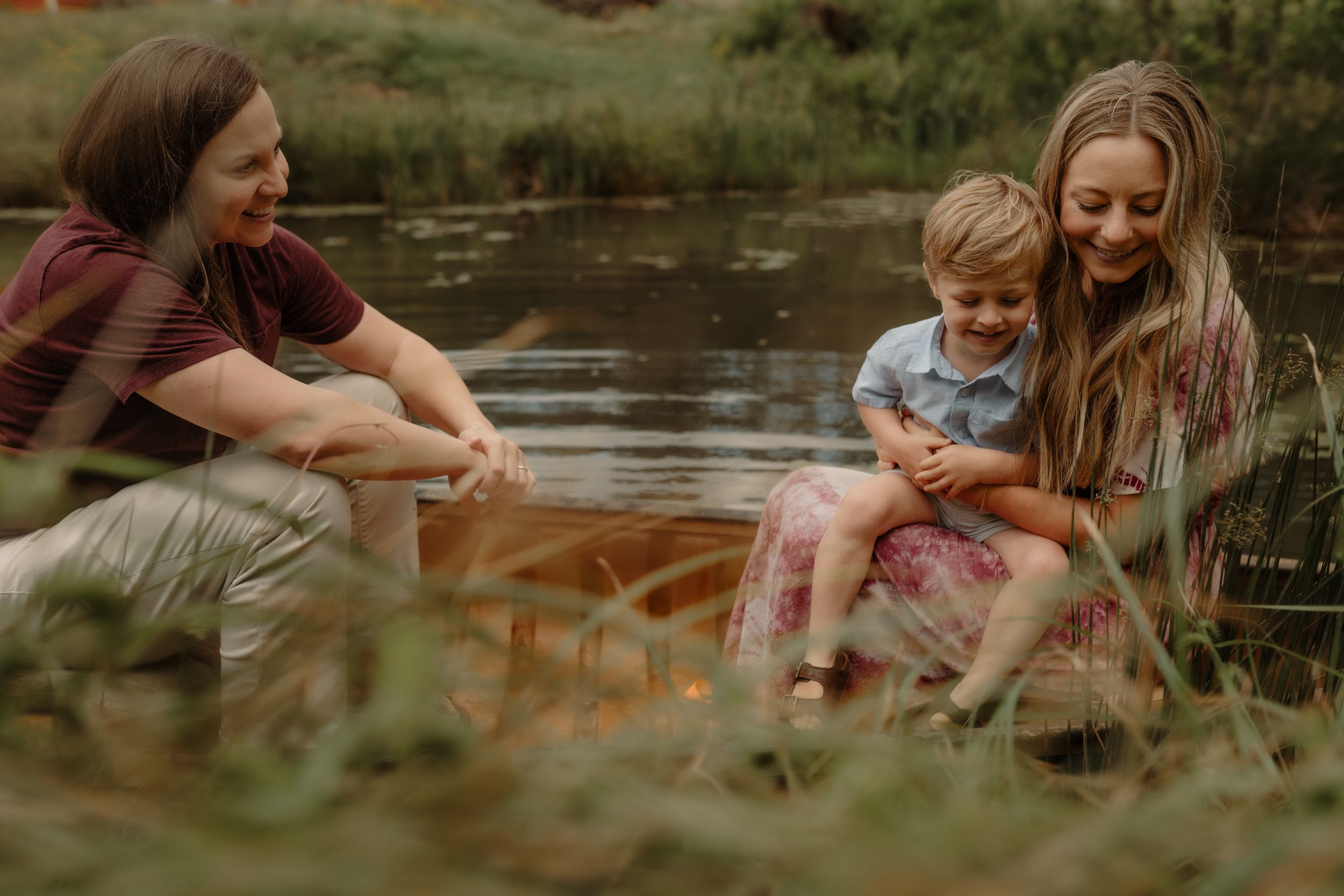 A family enjoys a peaceful moment together by a pond's edge surrounded by tall grass.