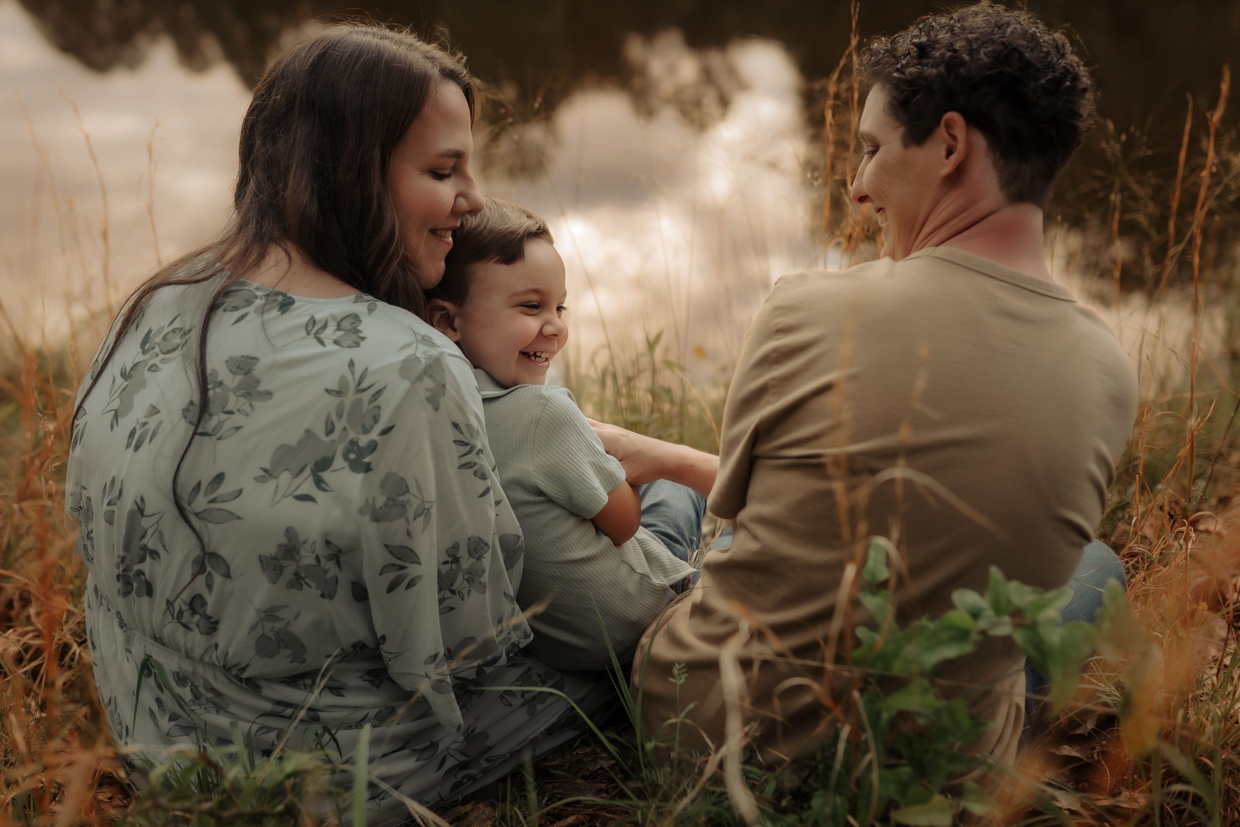 A family sits together in a golden field during sunset, sharing an intimate moment in nature.