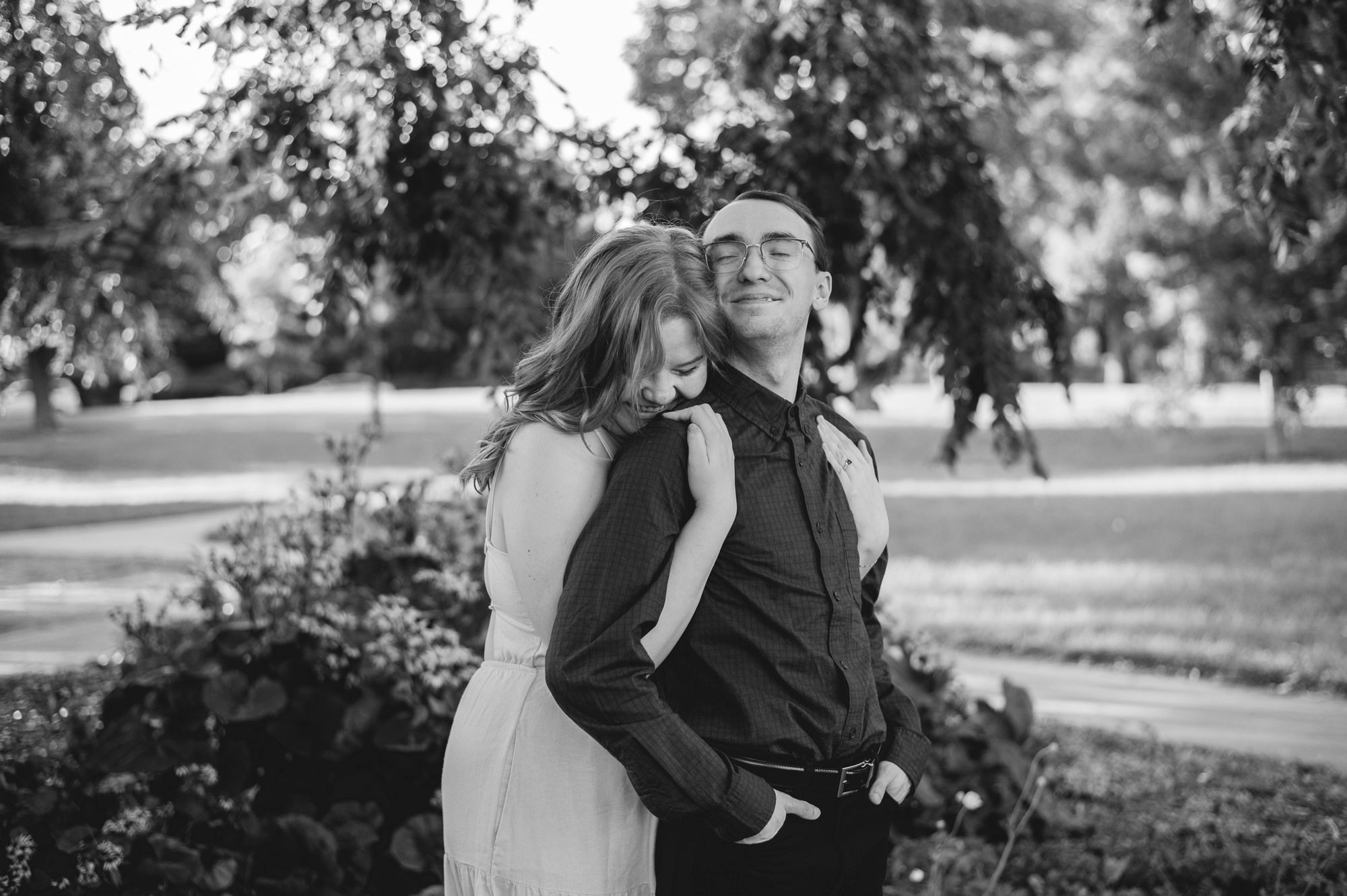An intimate black and white portrait captured in a peaceful park setting.