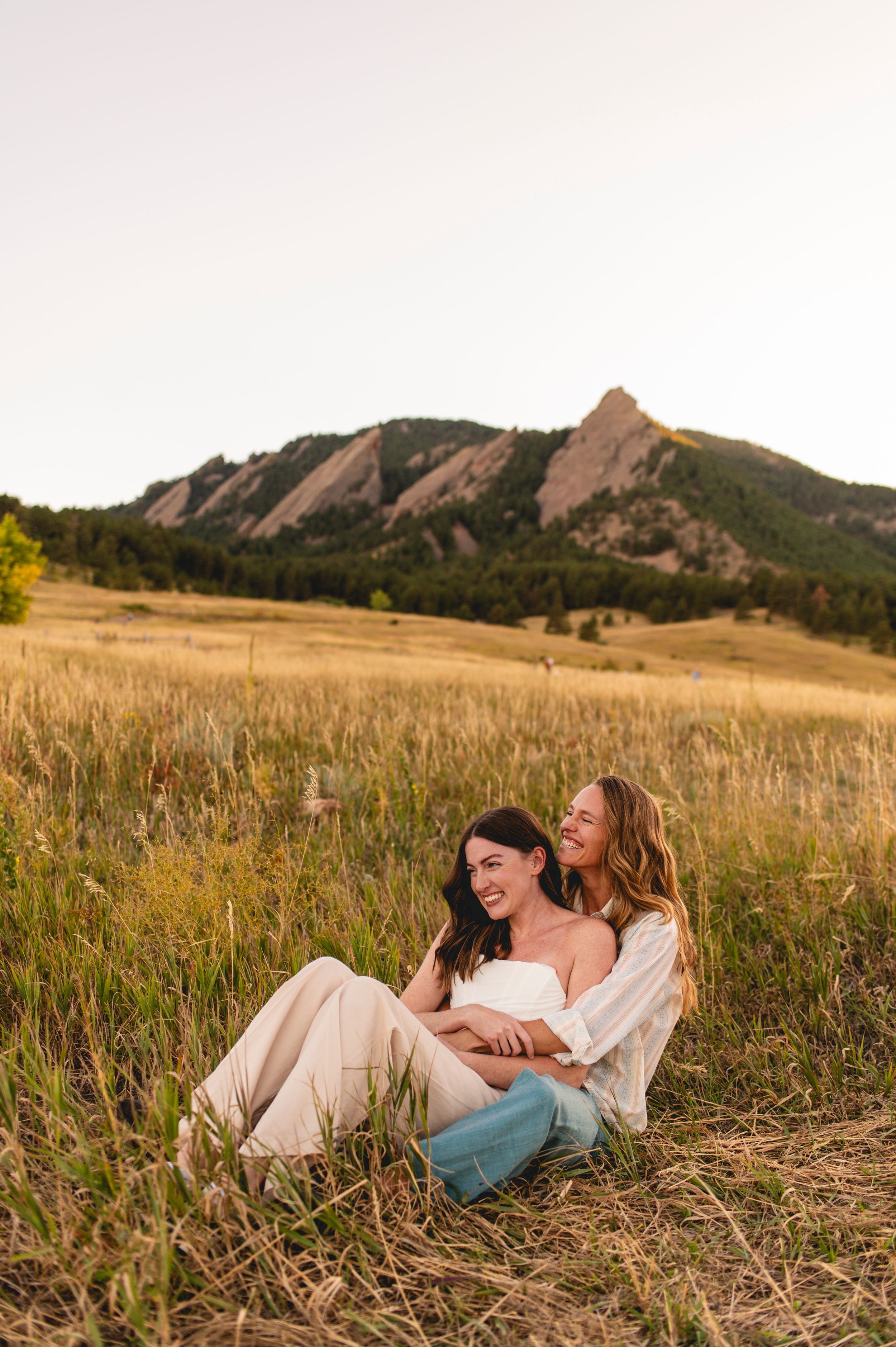 Two people share an intimate moment in a field with the Flatirons mountains of Boulder in the background.