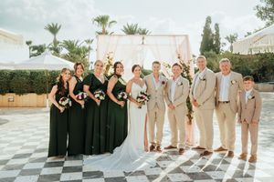 Wedding party members pose together in coordinating formal attire at an outdoor venue with palm trees in the background.